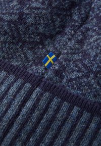 Kadar blizu strukturirane plave pletene tkanine s malo švedskom zastavicom ušivenom u materijal.
