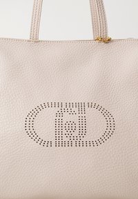 Borsa tote in pelle beige con un design ovale perforato. Texture liscia con doppi manici e dettagli in metallo color oro.