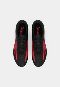 Μαύρα αθλητικά παπούτσια με κόκκινες ρίγες, υφή στην επάνω μεριά και αεροδυναμικό σχέδιο. Περιλαμβάνουν κορδόνια και κομψό προφίλ.
