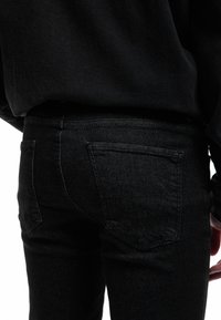 Jeans de mezclilla negra con un diseño ajustado, corte recto, bolsillos traseros y costuras de contraste en una textura suave y mate.