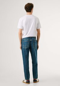 Hvid bomulds t-shirt og blå denim jeans med en afslappet pasform. Bemærkelsesværdige detaljer inkluderer to baglomme og kontrastsyet.
