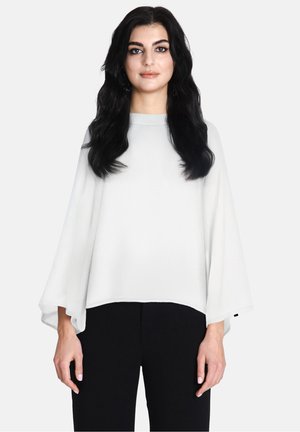 Blouse blanche fluide avec des manches chauve-souris et un col rond, fabriquée en tissu léger. Portée avec un pantalon noir.