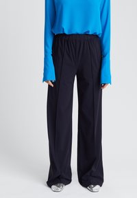 Zwarte wijde broek met plooien, gecombineerd met een lang-sleeve felblauw top. Geverfde zilveren schoenen maken de outfit af.