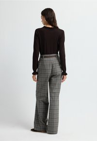 Top marrón de manga larga con un cuello fruncido, combinado con pantalones de pierna ancha a rayas grises de cintura alta y un cinturón marrón, visto desde la parte posterior.