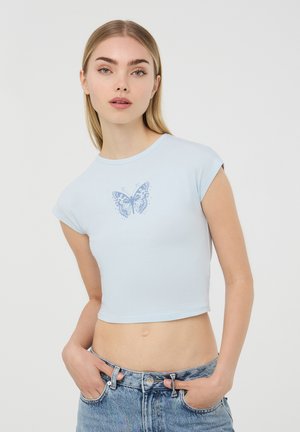 T-shirt cropped bluastro realizzato in cotone con maniche corte. Presenta una grafica di una farfalla in blu scuro al centro.