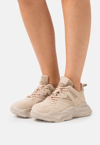 Beige sneakers med kraftig sula, i mocka och mesh-material, med orange snören, vadderad tung och sidor.