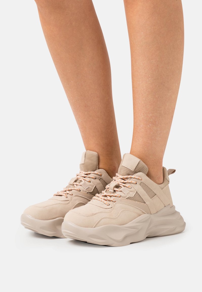 Beige sneakers med kraftig sula, i mocka och mesh-material, med orange snören, vadderad tung och sidor.