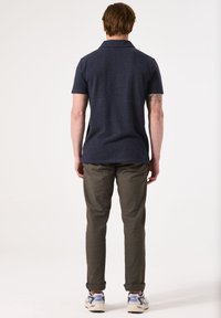 Marineblauw poloshirt met korte mouwen, gecombineerd met olijfgroene broek. De outfit omvat witte sneakers met blauwe accenten en een gestructureerde afwerking.