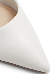 Valkoinen nahkainen kärkitossu, jossa on sileä pinta, matala leikkaus ja neutraali sisustus. Suunniteltu virtaviivaiseksi siluetiksi.