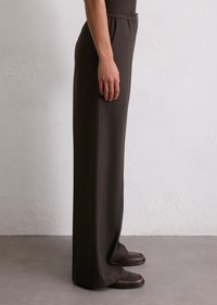 Bruine, high-waisted broek met een gladde textuur, wijde pijpen en een zijzak. Gecombineerd met donkere, casual schoenen.