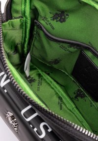 Svart väskas inredning med grön tygfoder som har svart randig textur och tryckta logodesign. Innehåller flera avdelningar och fickor.