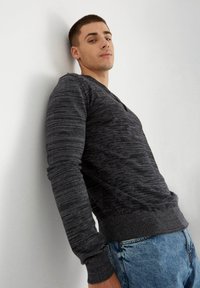 Suéter texturizado en gris oscuro con un cuello henley, puños y dobladillo acanalados, combinado con jeans de mezclilla azul claro.