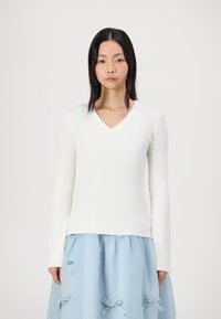 White ribbed long-sleeve top with a V-neck design, paired with a light blue skirt featuring bow accents and gathered texture.