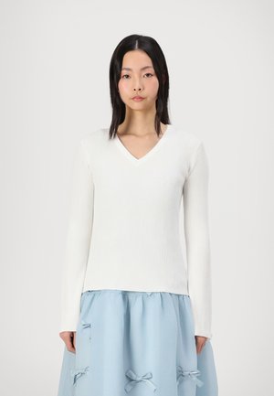 White ribbed long-sleeve top with a V-neck design, paired with a light blue skirt featuring bow accents and gathered texture.
