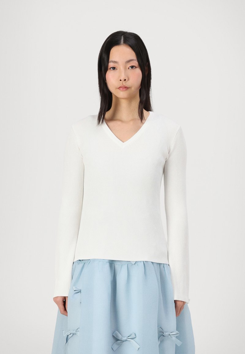 White ribbed long-sleeve top with a V-neck design, paired with a light blue skirt featuring bow accents and gathered texture.