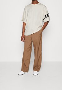 Ljusbeige oversized t-shirt med svarta ränder på ärmarna, kombinerad med bruna vida byxor och vita sneakers. Enkel design, avslappnad passform.