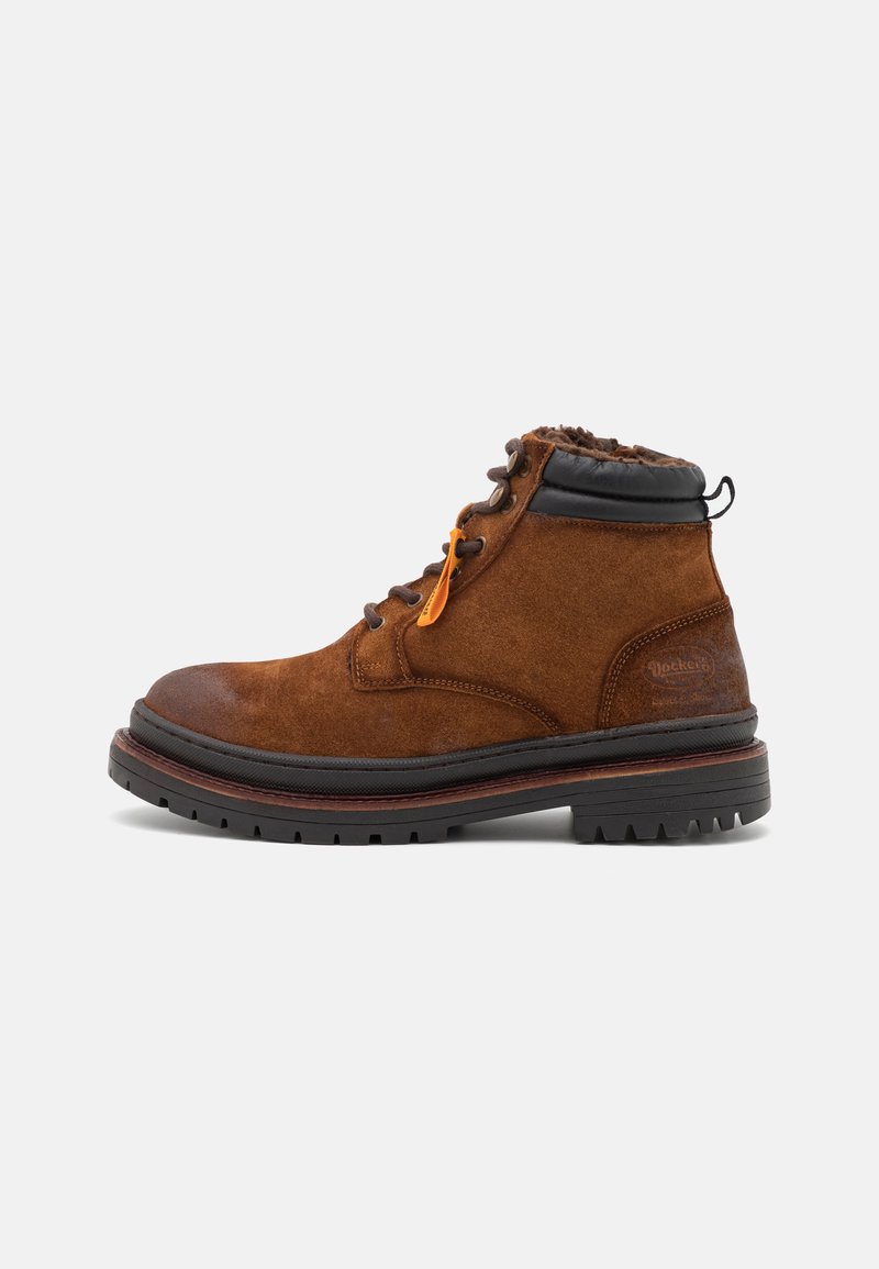Stivali alla caviglia in suede marrone con colletto in pelle nera, dotati di lacci arancioni e una suola in gomma testurizzata con scanalature profonde per una migliore aderenza.