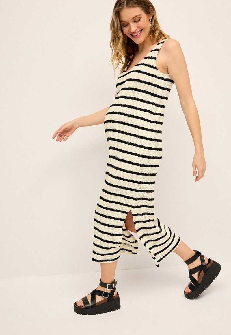 Gestreifter Strick-Maxikleid in Creme und Schwarz, mit V-Ausschnitt und Seitenschlitzen. Kombiniert mit klobigen schwarzen Plattform-Sandalen mit Knöchelriemen.