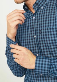 Niebiesko-czarna koszula na guziki w kratę z kołnierzykiem, wyposażona w kieszeń na piersi i prążkowane wewnętrzne mankiety. Wykonana z lekkiego materiału.