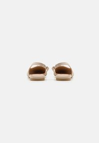 Sandalias beige con una textura lisa y mate, que cuentan con dos correas ajustables y una suela plana. Diseño minimalista, sin patrones o herrajes visibles.