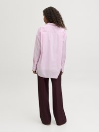 Long-sleeve, light pink shirt with a collar and buttoned cuffs, worn with dark burgundy, wide-leg trousers. Smooth fabric texture.