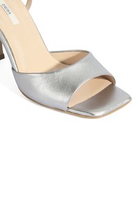 Silberne, metallische High-Heel-Sandalette mit offener, quadratischer Zehenpartie und breitem Riemen. Glatte Textur mit leichtem Glanz und Blockabsatz.