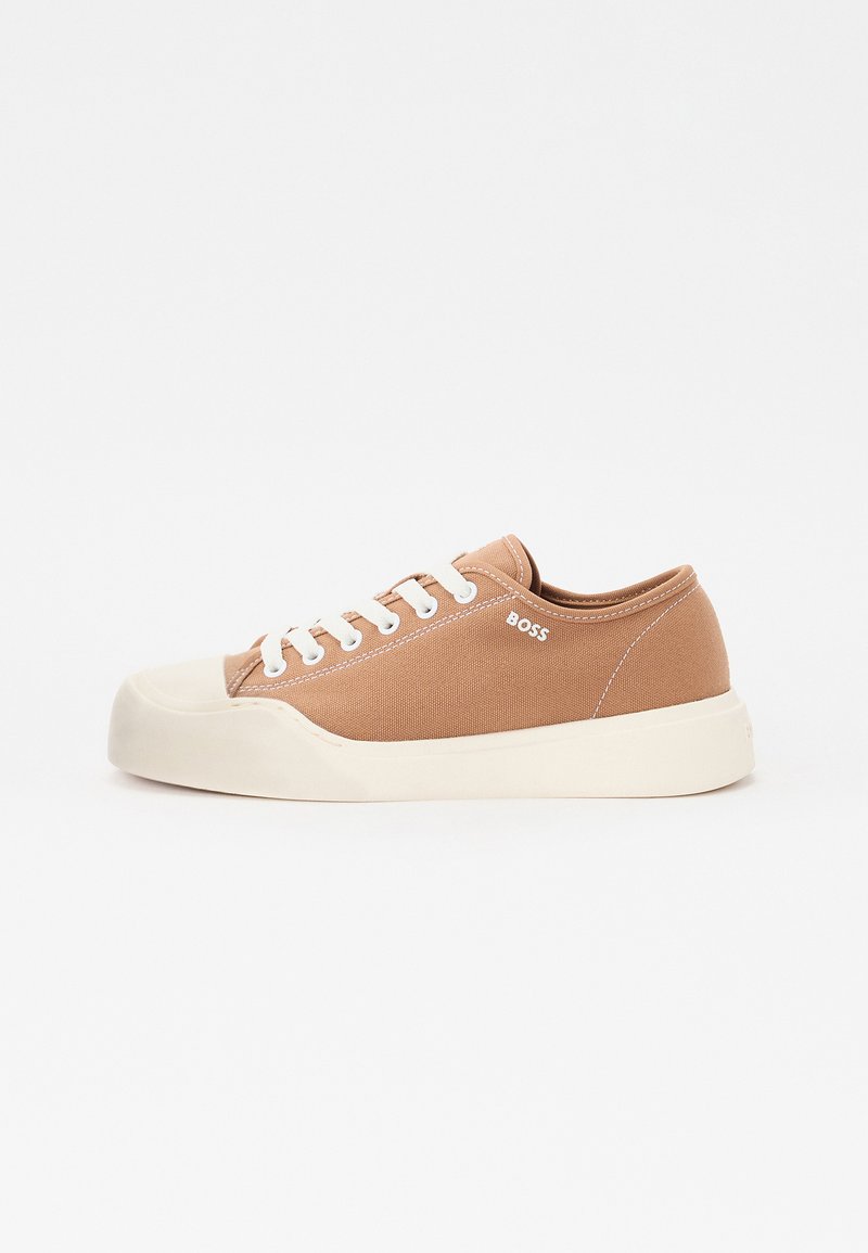 Baskets en toile beige avec semelle en caoutchouc, bout rond, lacets blancs et détail de logo sur le côté. Texture lisse avec des accents de couture contrastants.