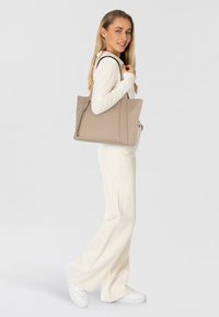 Sac cabas en cuir beige avec une forme structurée, dot�é d'une fermeture éclair sur le côté et de doubles poignées. Texture lisse, design minimaliste avec des accents subtils.