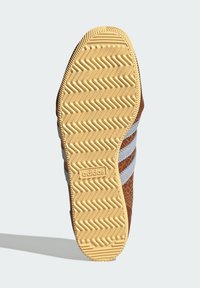 Gumowa podeszwa buta z bieżnikiem w zygzakowaty wzór. Brązowa i szara cholewka z teksturowanymi detalami. Logo Adidas widoczne z boku.