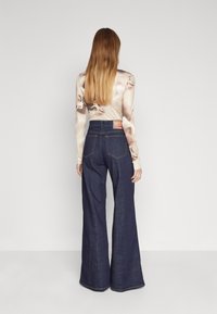 Dark blue wide-leg denim jeans with a high waist, featuring back pockets and a branded label on the waistband. Smooth texture and tailored design.