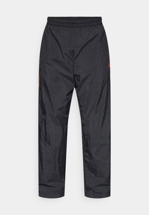 Pantalon de sport noir avec une ceinture élastique, fabriqué dans un matériau léger et texturé, avec un petit logo rouge sur le côté gauche.