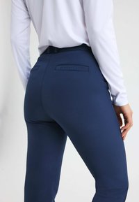 Mörkblåta figurnära byxor med en slät yta och en broderad logotyp på baksidan. Har två bakfickor och en medelhög midja.