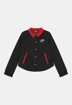 Veste noire Nike Air avec col rouge et bordures de poche rouges, fermeture avant à boutons pression et poignets élastiques sur les manches longues, posée à plat sur un fond blanc.
