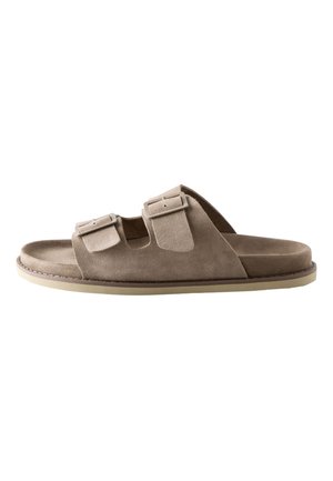 Sandalia tipo deslizador de ante beige con dos correas ajustables con hebilla y suela de goma plana, diseñada para uso casual.