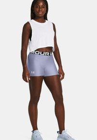 Svijetloplavi kompresijski šorts s crnim pojasom "UNDER ARMOUR", uparen s bijelim bezrukavnim crop topom. Vidljive sportske cipele.
