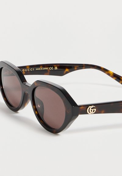 Lunettes de soleil œil-de-chat écaille avec verres marron et logo Gucci doré sur la branche, fabriquées au Japon.