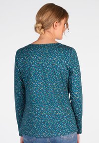 Langärmliges türkisfarbenes Hemd mit einem bunten Blatt- und Beerenmuster, runder Ausschnitt und taillierter Form. Weicher Stoff und elastisches Material.