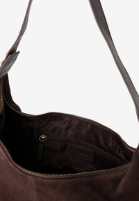 Sac à main en daim marron avec une large ouverture, fermeture éclair et poche intérieure. Texture douce et bandoulière lisse. Intérieur doublé de tissu foncé.