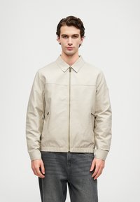 Šviesiai kremas švarkas su užtrauktuku priekyje ir apykakle, su dviem šoninėmis kišenėmis. Pagamintas iš lygaus audinio, su elastingomis rankogaliais ir apatine dalimi.