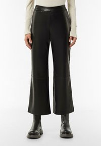 Zwarte faux leren wijde broek met een hoge taille, voorzien van stiksel-details en een gladde textuur. Gecombineerd met robuuste zwarte laarzen.