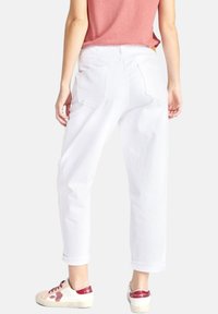 Witte denim broek met een relaxte pasvorm, vijf zakken en zichtbare stiksels. Geddragen met een roze t-shirt en witte sneakers met rode accenten.