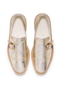 Gyllene läderskor med slip-on design, spänndetalj, perforerade accenter och ljusbruna kanter. Tillverkade av Cole Haan. Slät textur.