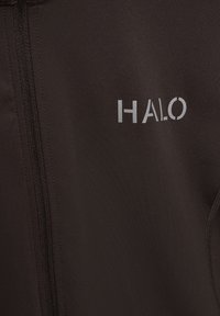 Svart stretchtygjacka med dragkedja framtill, med en reflektiv "HALO"-logotyp på övre vänstra sidan och texturerade detaljer på sidan.