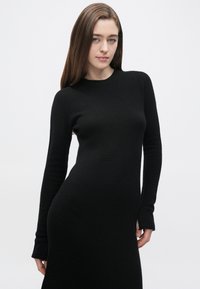 Czarna sukienka z długim rękawem wykonana z miękkiej, teksturowanej dzianiny. Posiada okrągły dekolt i dopasowany fason z rozkloszowanymi rękawami.