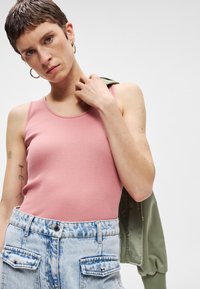 Ροζ ριμπ μπλουζάκι με λεπτές τιράντες, συνδυασμένο με ψηλόμεσα ανοιχτό γαλάζια τζιν σορτσάκια με λεπτομέρειες τσέπης και ασημένιες καρφίτσες, πράσινο μπουφάν.