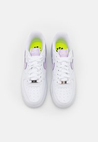 Paire de baskets blanches Nike Air Force 1 avec un logo swoosh violet clair et des semelles intérieures jaune néon, vues de dessus sur un fond blanc.