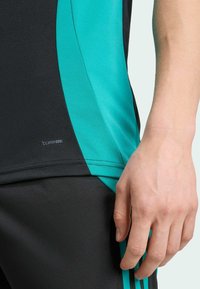 Camisa deportiva negra con acentos turquesa, que presenta una textura elegante y suave con el branding "CLIMACOOL" cerca del dobladillo.