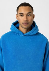 Blauwe hoodie met een zachte textuur, oversized ontwerp en een trekkoordcapuchon. Bevat een kangoeroezak en gebreide manchetten.