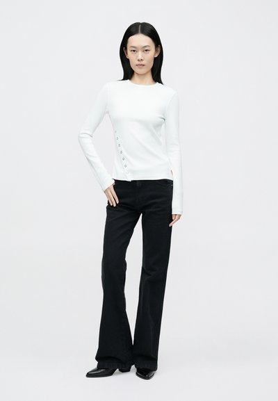 Haut blanc à manches longues avec détails de boutons sur le côté; associé à un pantalon noir évasé; tissu lisse avec une silhouette ajustée.