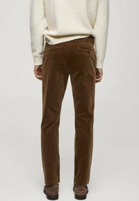 Pantalon en velours côtelé marron à coupe droite, avec deux poches arrière et une texture côtelée subtile, associé à un pull léger en maille.